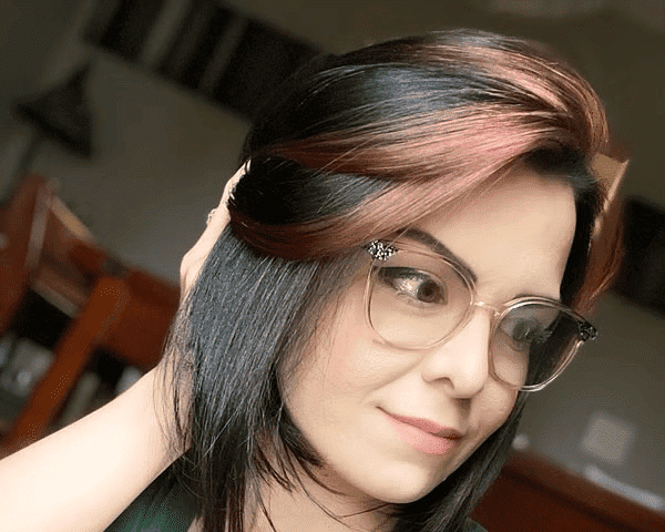 Young woman with glasses and short hair, wearing a green shirt, looks off-camera indoors.