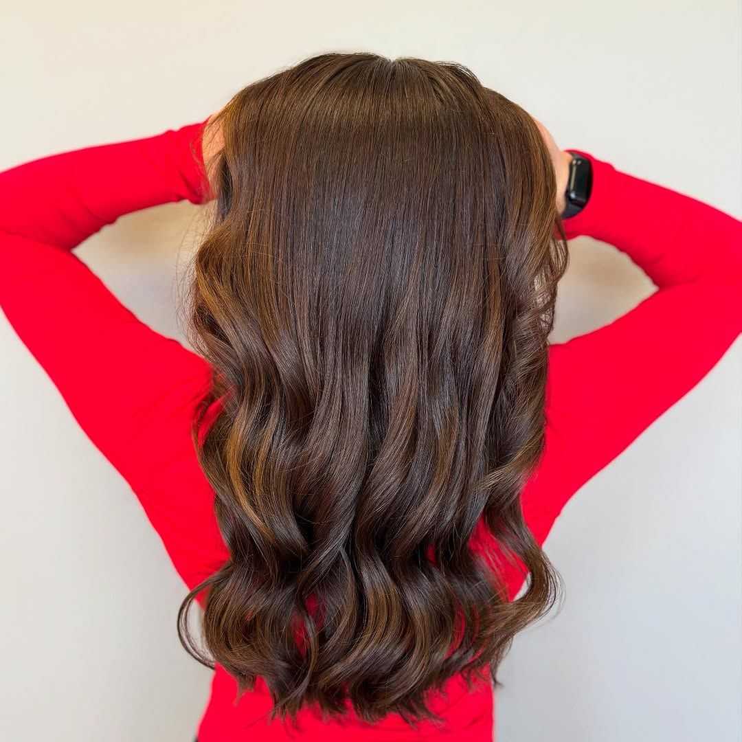Brown-haired person in red top with loose waves, viewed from behind.
