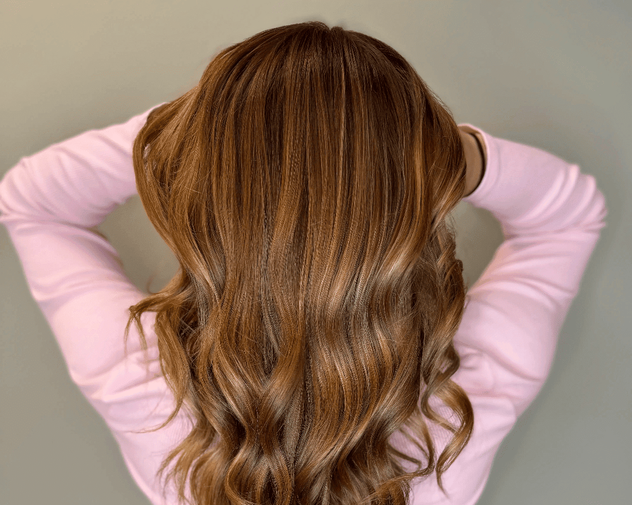 Wavy brown hair styled down, seen from the back, with a person in a pink top.