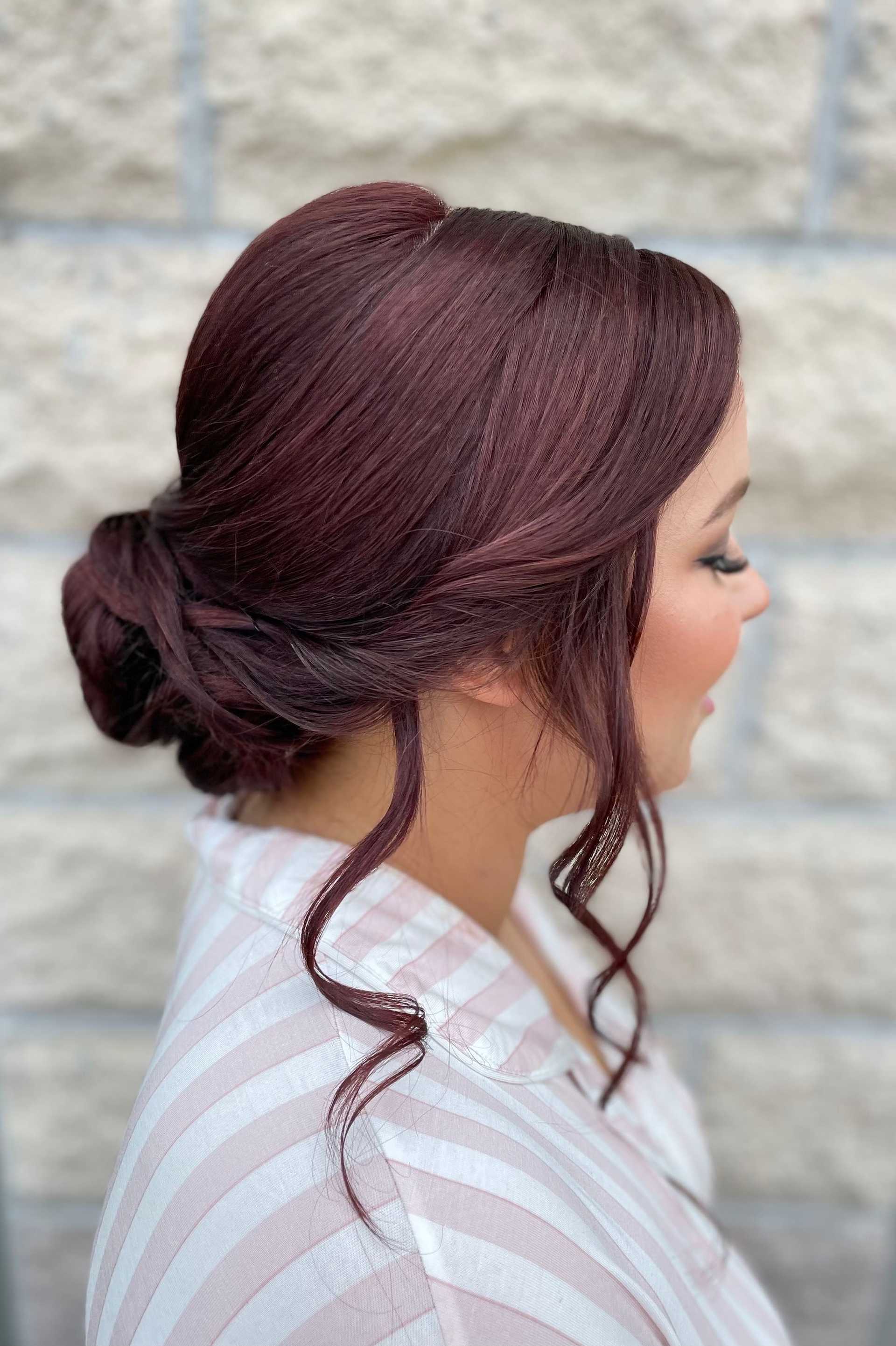 Woman with styled brunette hair in a bun, wearing a striped shirt, against a stone wall.
